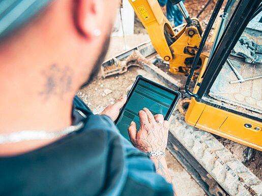 Mitarbeiter nutzt ein Tablet auf einer Baustelle neben einem Bagger