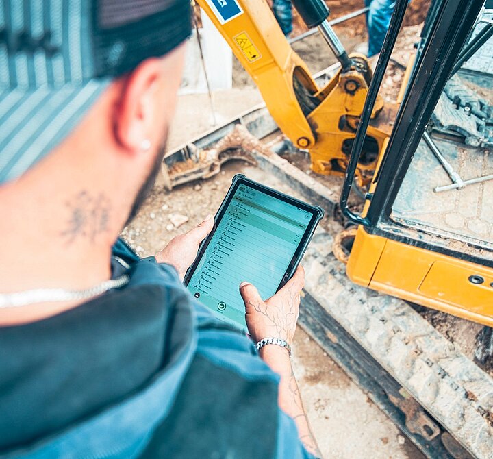 Digitale Baustellendaten auf einem Tablet neben einem Bagger